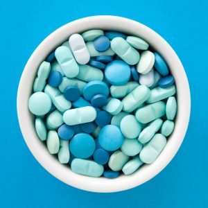 White bowl filled with blue pills on blue background